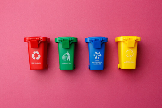 Waste separation, garbage sorting. Colorful garbage containers for sorting waste. Garbage containers for paper, plastic, glass and organic garbage. Four colorful dumpsters stand on a pink background.