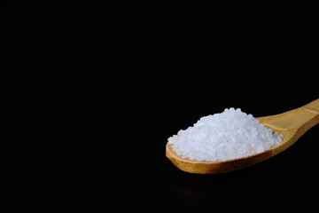 Crystal mineral salt in wooden spoon against black background