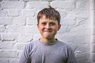 Fototapeta premium boy smiling. funny teenager snails against the background of brick wall. teen boy with pursed lips and worried facial expression. Nervous tension, bad feelings and stress.Child emootion