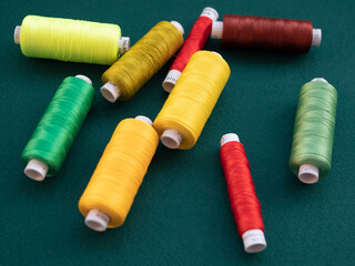 Spools of multicolored thread for sewing and embroidery on the green background. Threads for sewing machine and overlock in the atelier