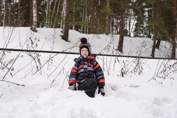 Fototapeta na wymiar Little child boy in the winter in the forest park plays with snow.