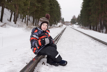 Fototapeta na wymiar little child boy sitting on the railroad in winter plays with snow.