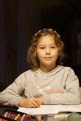 Fototapeta na wymiar Junges Mädchen macht Hausaufgaben. Sie sitzt zuhause an einem Tisch. Es ist schon spät. Der Hintergrund ist dunkel, das Mädchen ist hell. 