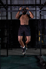 afro american shirtless sportsman pull up on horizontal bar in modern black gym, full-length portrait. strong muscular male is engaged in sport, fitness training alone indoors, exercising