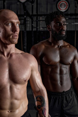 Fototapeta na wymiar Workout. Crossfit. Extreme. Training. Portrait of two interracial shirtless sportsmen before or after cross fit training, strong men with perfect body, abs muscles. focus on black man in background