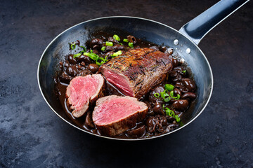Traditional fried dry aged angus beef filet roast and medaillon natural with mushrooms in red wine sauce served as close-up in a classic skillet