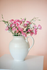 Bouquet with eustoma, summer flowers in a white vase, on a pink-beige background.