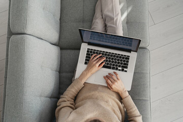 Businesswoman work on laptop lying on comfortable couch in office or at home. Successful business lady reading document, report or email from partner sitting on sofa remotely on quarantine, top view