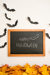 A sign saying 'Happy Halloween' surrounded by black bat and orange leaves. Blackboard for halloween lettering. Modern halloween bats background. Halloween day composition. Party greeting card