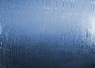 The blue sky shines through the misted window with dripping drops of water