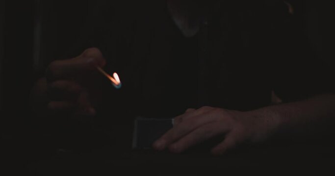 Dark scene with hand's of unrecognizable man who firstly ignite's match before black candle. Quiet moves of a man in a dark room creates atmosphere of romantic ancient rituals or augury