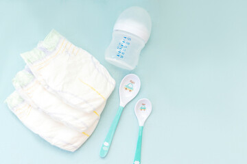 Baby's stuff with copy space. diapers with bottle for milk and spoons on blue background. Newborn, infant, baby shower gifts, healthcare concept