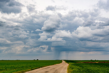 landscape with dark sky with rain clouds before storm in green field with gravel road. thunderstorm front