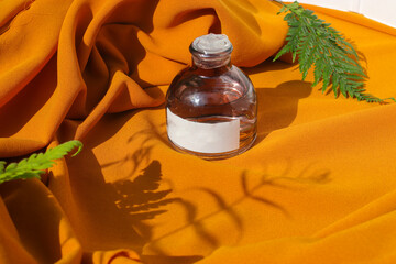 50 ml Perfume bottle with blank white label and green leaves on textured orange fabric background. Perfume bottle stock photo