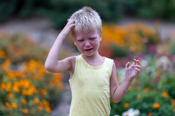 Funny blond child in yellow t-shirt crying among flowers