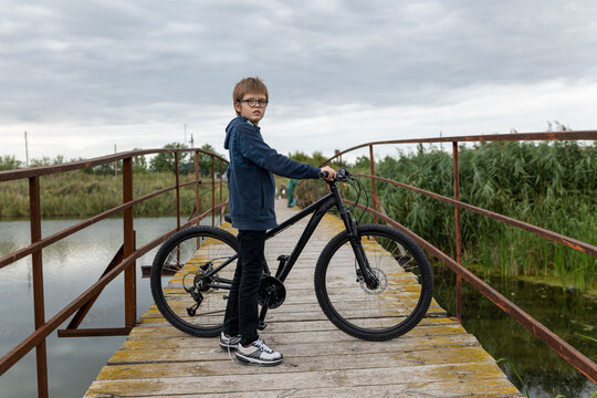 Funny boy in glasses posing on bicycle on bridge over river