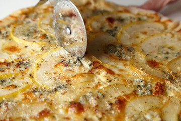 Chef cutting pear fruit pizza with knife on wooden board closeup