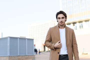 Young man in coat and white t-shirt looking at camera outdoors 