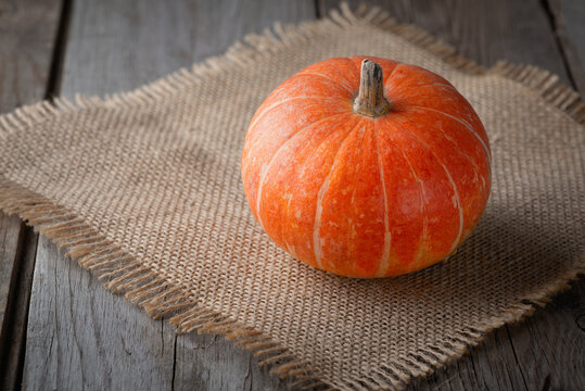 Orange pumpkin with a ponytail on burlap. Wooden background. Food, autumn, holiday, thanksgiving, harvest season concept