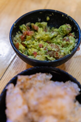 Bowls of pork rinds and guacamole on wooden surface