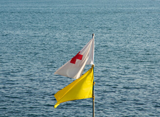 Fototapeta premium two rescue flags yellow and white with a red cross on the background of the sea