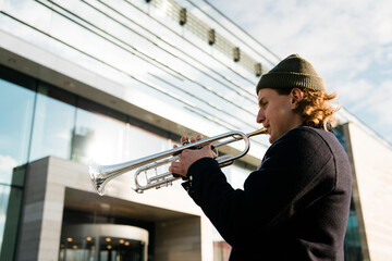 A man with a hat playing a trumpet on modern city background. Male Jazz musician play music on city...