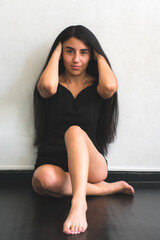 Fototapeta na wymiar Latin woman posing in a black blouse. feminine identity: confident young woman sitting on the floor of her house. Colombian posing to the camera