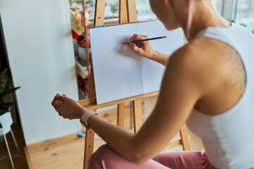 Obraz premium Woman artist draws picture on white paper with graphite pencil at wooden easel in light studio