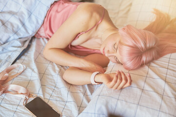 Obraz na płótnie Canvas Tired woman with pink hair sleeps with mobile phone in comfortable bed at home