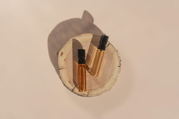 Two glass perfume samples on a wooden tree tray lying on a beige background. Luxury and natural cosmetics presentation. Testers on a wood cut in the sunlight. Top view