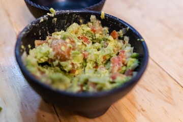 Black bowl of delicious guacamole on a wooden surface