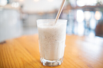 Milkshake with straw in glass above wooden table
