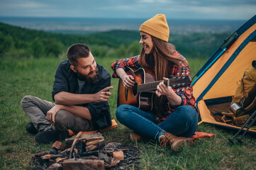 Couple of campers spending time together in the nature while playing guitar