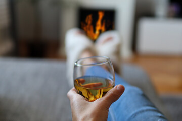 Female hand holding a glass of wine and lies in bed and relaxing next to the fireplace on a cold winter day