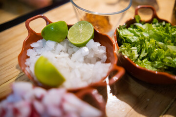 Clay pots of chopped radishes, onions, lettuce, and limes on wooden table