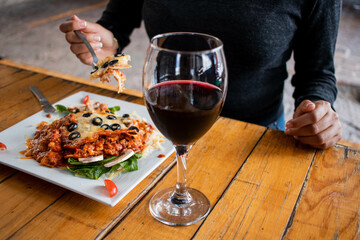 Comiendo lasagna con copa de vino 