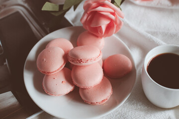 Pink macaron cookies with cup of coffee and rose flowers on white background. Spring still life scene. Vintage pastel styled photo. Copy space for you text. Toned image.