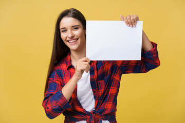Fototapeta na wymiar Smiling young woman holding white paper sheet. Studio portrait on yellow background.