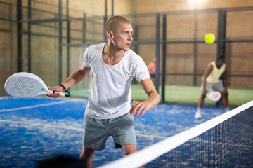 Concentrated man padel player hitting ball with a racket on a hard court