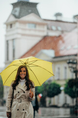 Woman wearing a yellow umbrella and walking during a heavy rain in the city