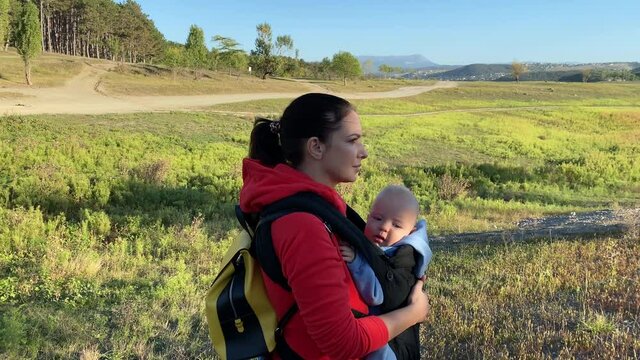 Woman with a baby in a sling ergo backpack traveling outdoor, family vacations adventure, mom with baby boy in infant kid carrier hiking. High quality 4k footage