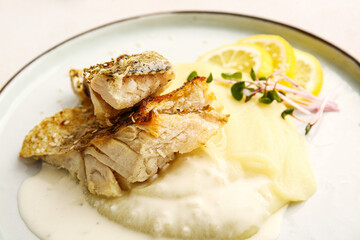 Plate with tasty baked cod fillet, sauce and mashed potatoes on light background, closeup