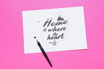 Paper with text HOME IS WHERE THE HEART IS and nib pen on pink background