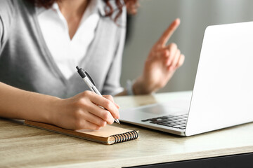 Young woman writing notes during online job interview at home