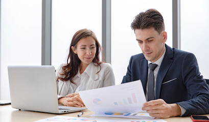 Obraz premium Happy Caucasian businessman and businesswoman officer staff employee in formal business suit sitting talking funny smiling laughing together at office workplace. Reading paperwork analysis report