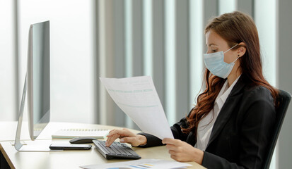Caucasian businesswoman entrepreneur owner in formal suit with hygiene safety face mask sitting holding analysis statistic paperwork document target report. Typing data with PC computer keyboard