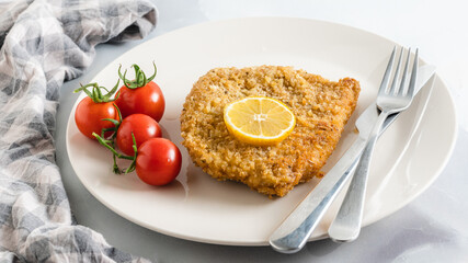 Crispy pan fried breaded pork chops served with lemon and fresh tomatoes close up on a plate