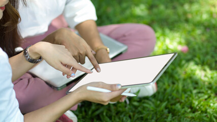 Cropped image of two of female friends sits in a city park looking on digital tablet