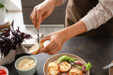Woman spreading toast with dip at table in kitchen