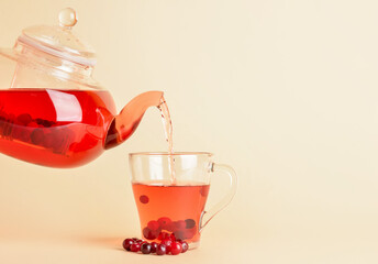 Pouring of tasty cranberry tea from teapot into cup on color background, closeup